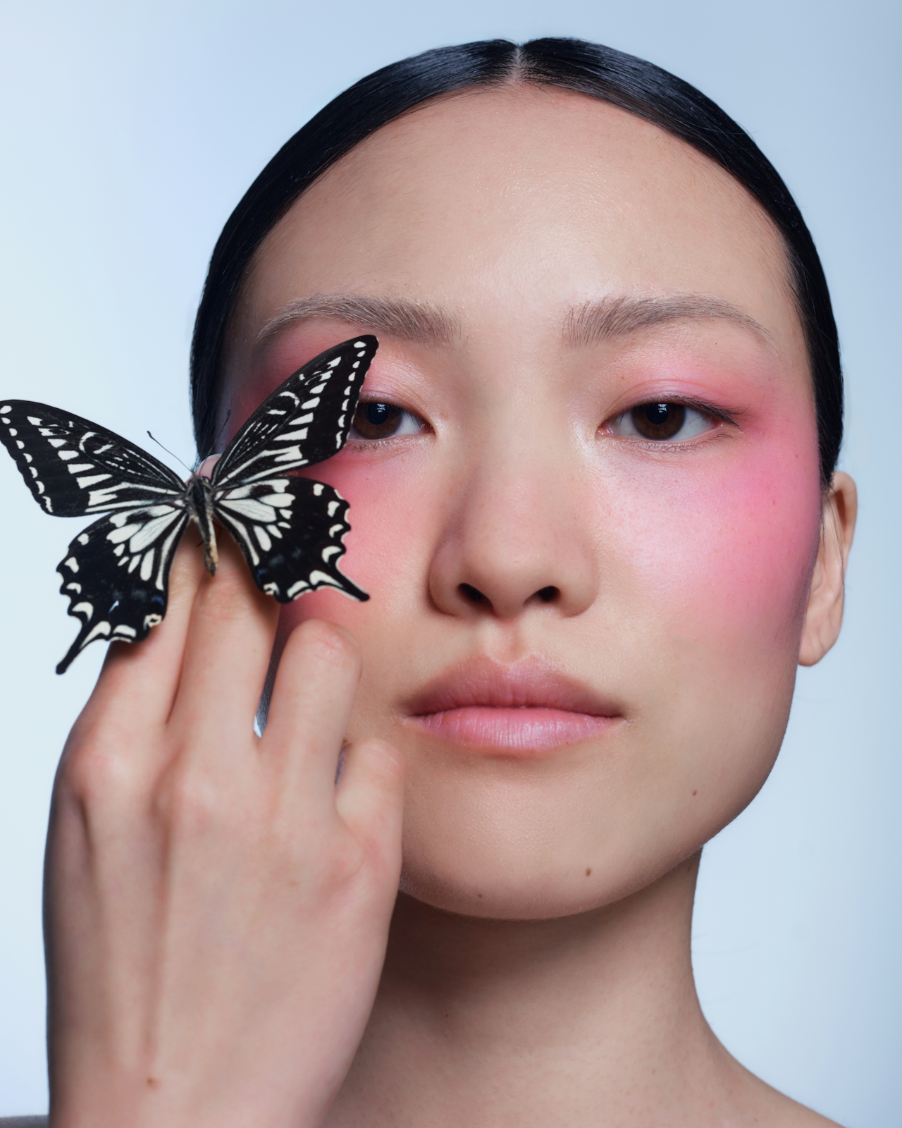Retrato editorial con mariposa negra sobre la mano — mirada directa